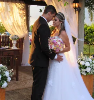 Cerimônia de casamento no pergolado de madeira com cortinas brancas e arranjos de flores