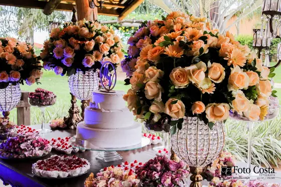 Mesa de doces com arranjos altos de rosas alaranjadas