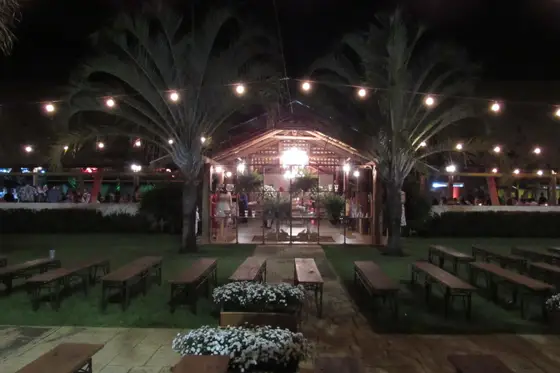 Salão à noite iluminado por varal de luzes, com bancos de madeira