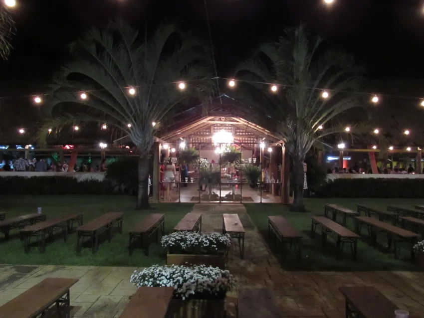 Salão à noite iluminado por varal de luzes, com bancos de madeira