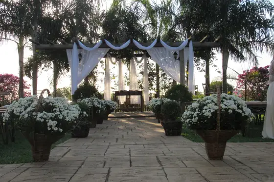 Altar de cerimônia ao ar livre com cortinas brancas e vasos de flores