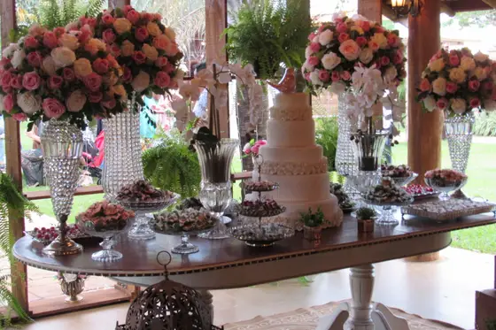 Mesa de doces com arranjos altos de rosas