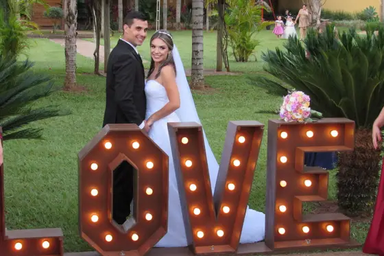 Casal de noivos ao lado do letreiro “LOVE” no jardim