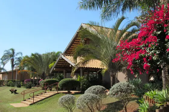 Fachada da sede com telhado de barro, jardim e árvores floridas