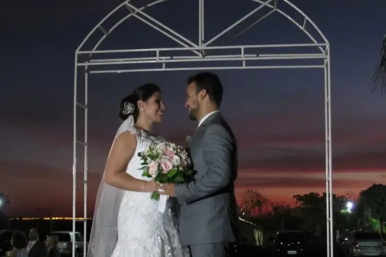 Casal de noivos sob arco metálico no fim da tarde